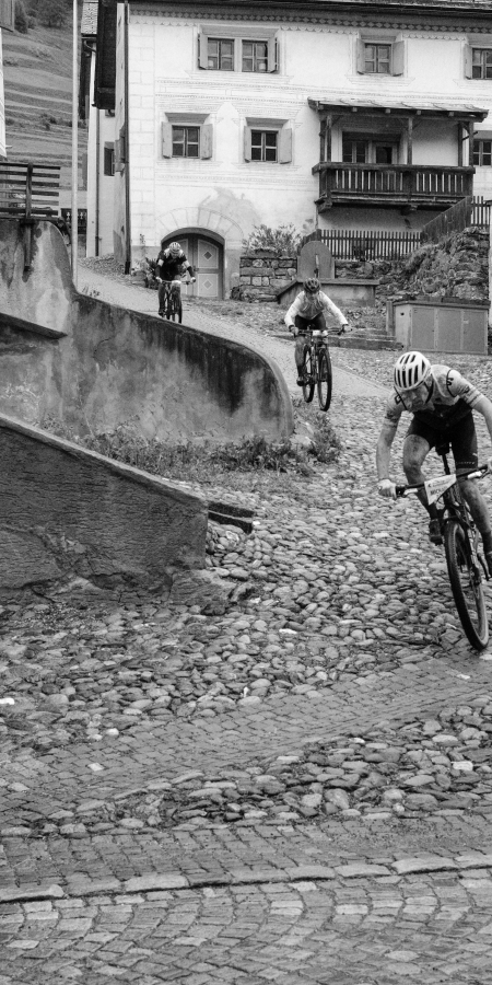 Rennradfahrer fährt während eines Radrennens über eine steile Kopfsteinpflasterstraße in einem historischen Dorf.
