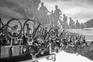 Gruppe von Radfahrern mit Rennrädern, deren Spiegelbild sich in einer Pfütze zeigt.